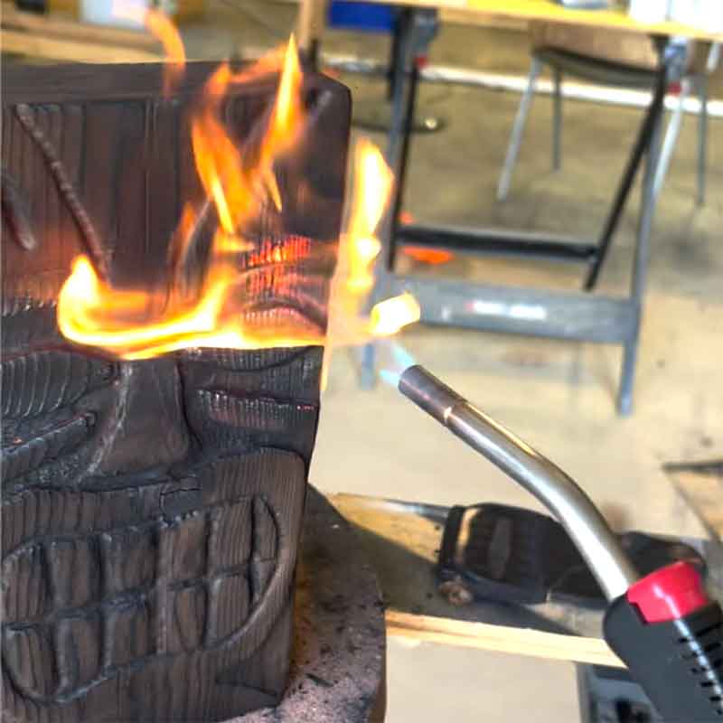 Using a flaming torch on a tiki carving